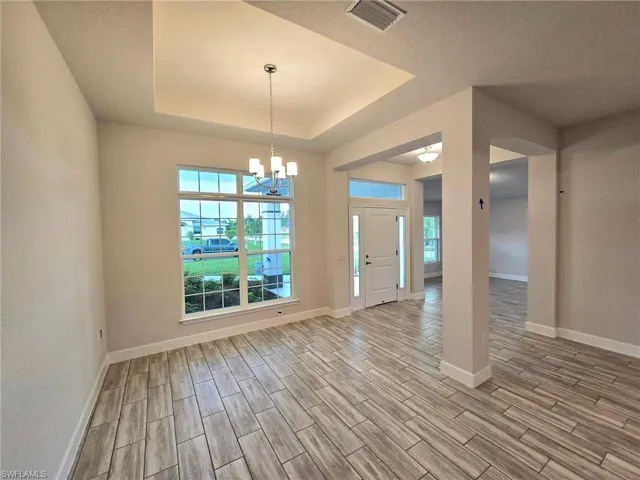 Empty room with a notable chandelier, light hardwood / wood-style floors, a raised ceiling, and a textured ceiling