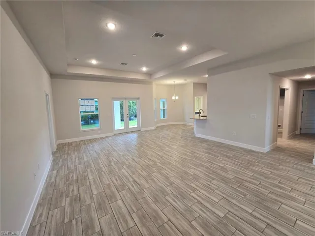 Unfurnished living room with a chandelier, light wood-type flooring, and a raised ceiling