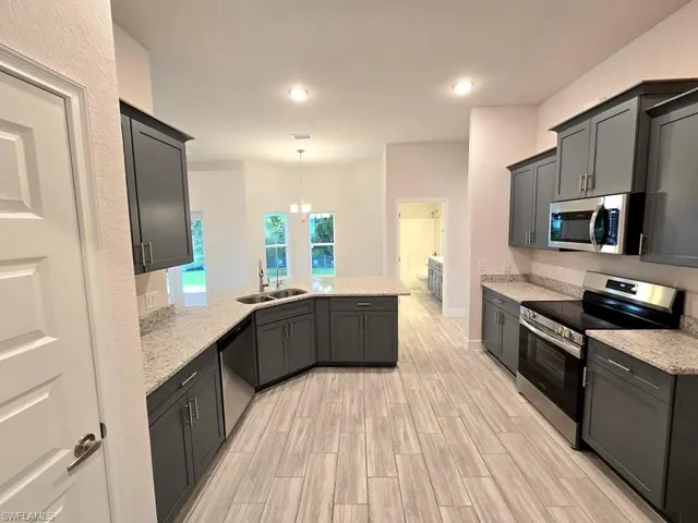 Kitchen featuring appliances with stainless steel finishes, light stone countertops, sink, and pendant lighting