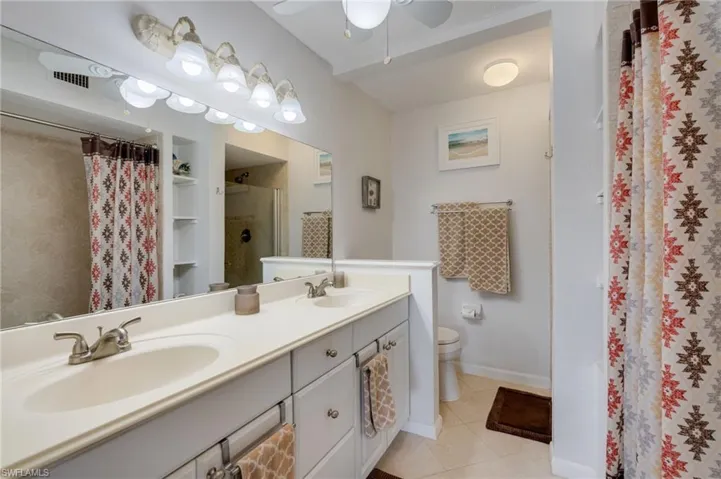 Bathroom with double vanity, a shower with curtain, light tile patterned flooring, and a ceiling fan