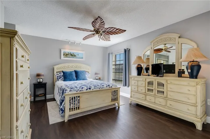 Bedroom with dark wood finished floors, a textured ceiling, rail lighting, and ceiling fan
