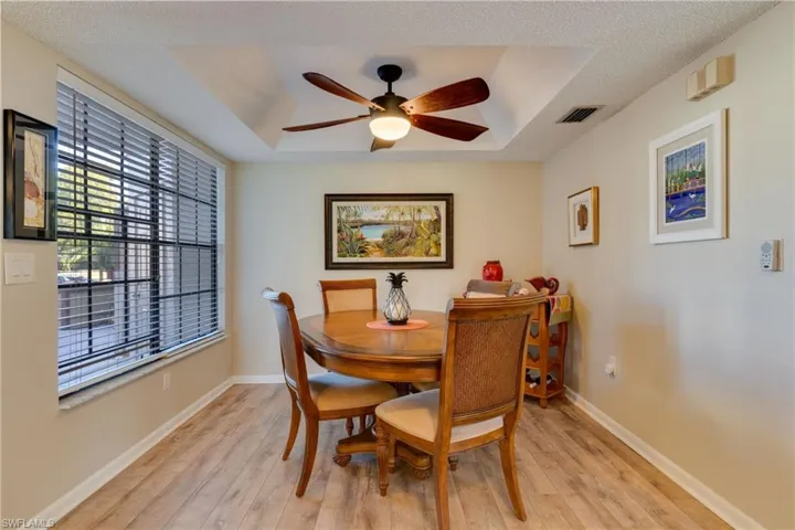 Dining area with light wood finished floors, a raised ceiling, a ceiling fan, and a textured ceiling