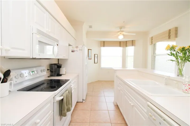 Kitchen featuring light tile patterned flooring, white appliances, white cabinetry, and sink