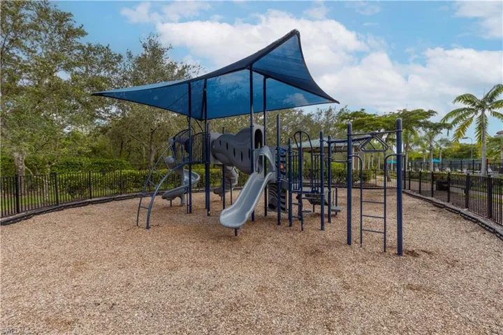 Outdoor playground featuring a shaded structure, slides, climbing elements, and a wood chip surface