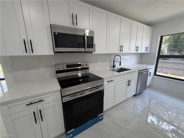 Contemporary kitchen featuring white shaker cabinetry, stainless steel appliances, light-toned countertops, a matte black faucet, and large format polished floor tiles