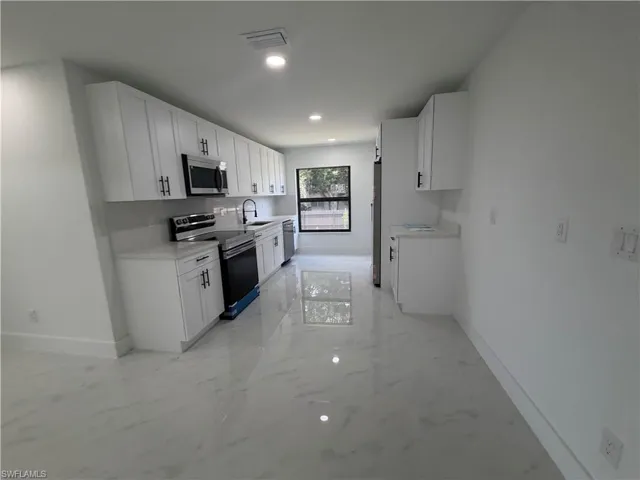Contemporary kitchen featuring white cabinetry, light countertops, subway tile backsplash, stainless steel appliances, and a window with a dark frame