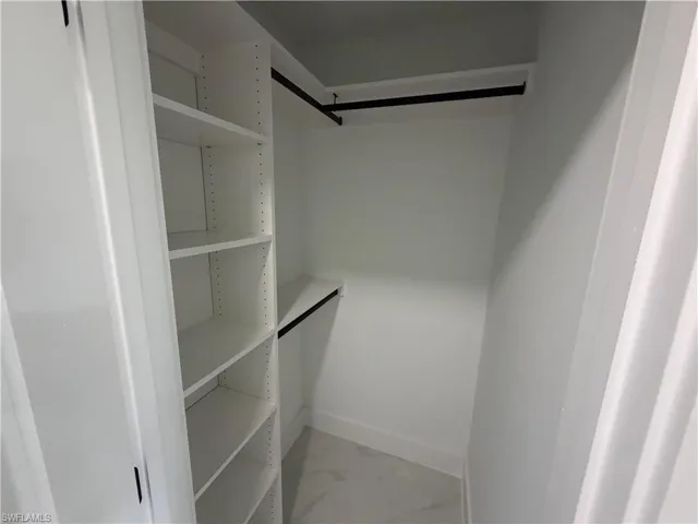 Built-in closet system featuring white shelving units, black hanging rods, and light-toned tile flooring