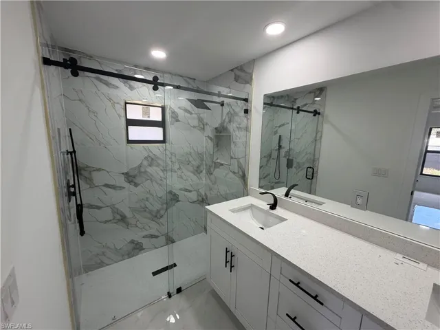 Spacious bathroom featuring a frameless glass shower enclosure with a sliding barn door system, white marble-look tile, and matte black fixtures