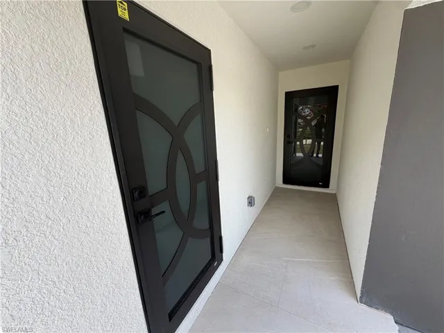 Contemporary entryway featuring an ornate dark-framed glass door, recessed ceiling lighting, textured stucco walls, and large format tile flooring