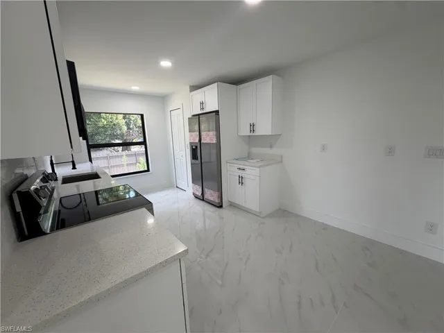 Contemporary kitchen featuring white cabinetry, light-toned countertops, a built-in electric cooktop, and a stainless steel refrigerator