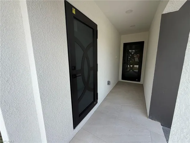 Entryway featuring two black security doors with geometric patterns, textured white stucco walls, and light-toned tile flooring