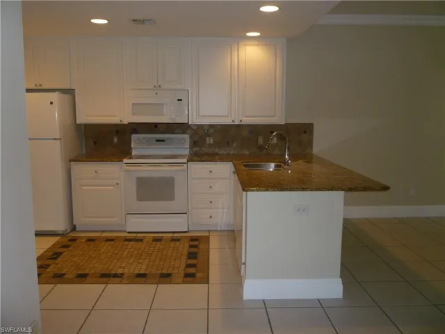 Kitchen featuring dark  granite countertops, inlaid flooring, white appliances, white cabinetry, a peninsula, and tasteful backsplash