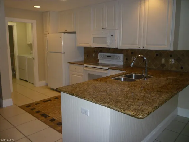 Kitchen featuring light tile patterned floors, white cabinetry, white appliances, backsplash, and a peninsula