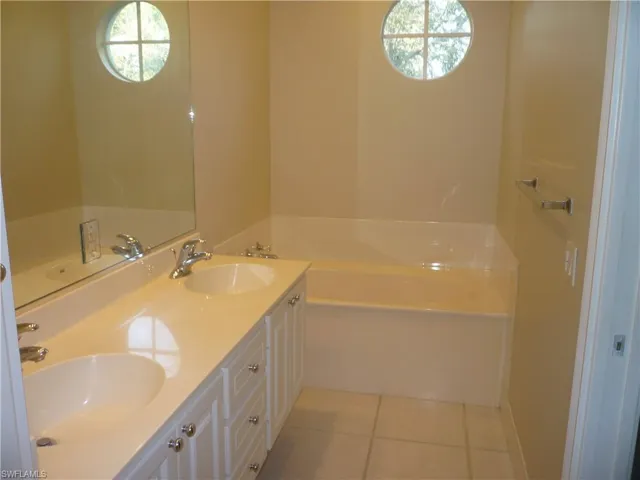 Tub side of master bathroom with light tile flooring and double vanity