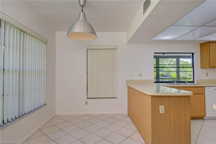 Kitchen featuring light tile patterned flooring, a peninsula, light countertops, dishwasher, and pendant lighting