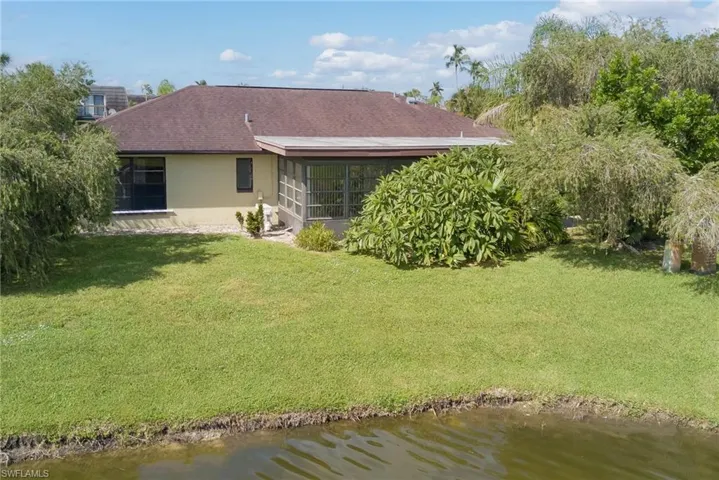 Back of house with stucco siding, a lawn, a water view, and a sunroom