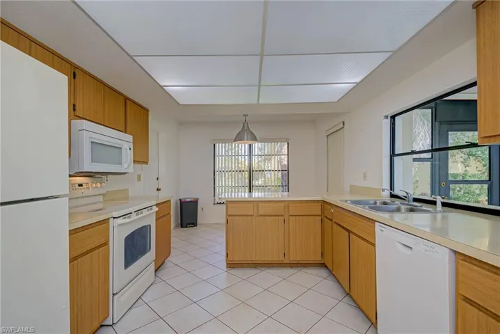 Kitchen with white appliances, light countertops, light tile patterned floors, a peninsula, and decorative light fixtures