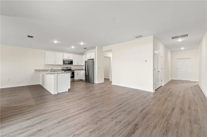 Kitchen with open floor plan, a peninsula, white cabinetry, appliances with stainless steel finishes, and light wood-style flooring