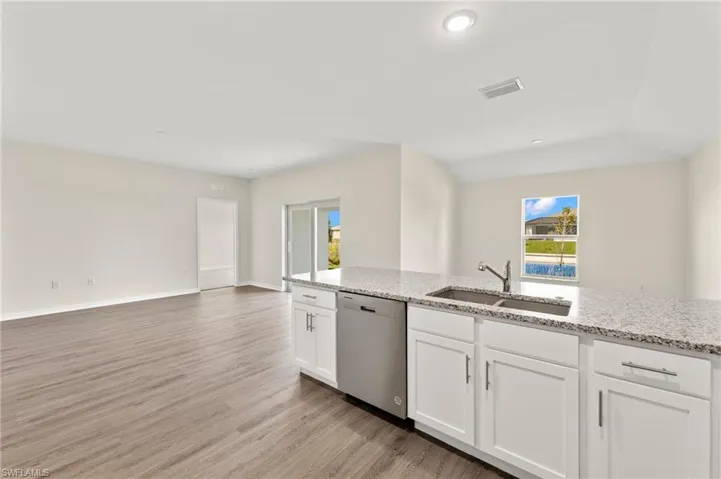 Kitchen with open floor plan, stainless steel dishwasher, light wood-type flooring, white cabinetry, and light stone counters