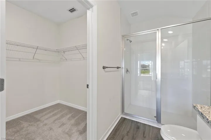 Full bathroom featuring a walk in closet, a stall shower, vanity, and light wood-style floors
