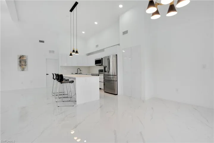 Kitchen featuring a towering ceiling, light countertops, appliances with stainless steel finishes, decorative light fixtures, and white cabinetry