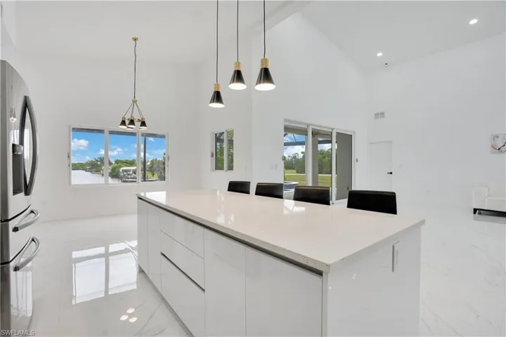 Kitchen with modern cabinets, white cabinetry, decorative light fixtures, light stone counters, and plenty of natural light