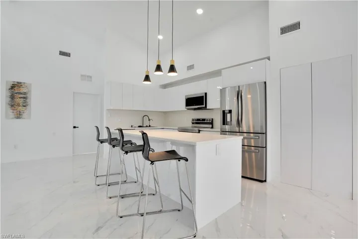 Kitchen featuring stainless steel appliances, a high ceiling, white cabinetry, decorative light fixtures, and a kitchen breakfast bar