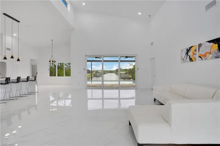 Living room featuring light marble finish floors, plenty of natural light, high vaulted ceiling, a water view, and recessed lighting
