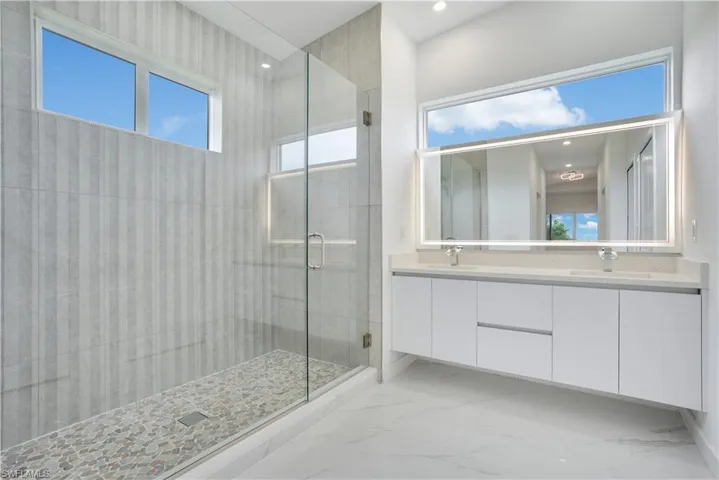 Full bath with double vanity, a stall shower, light marble finish flooring, and recessed lighting