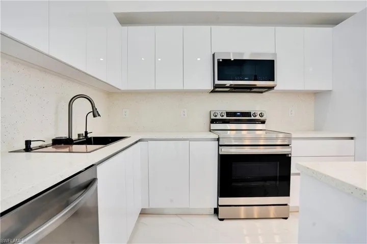 Kitchen featuring modern cabinets, appliances with stainless steel finishes, decorative backsplash, and white cabinets