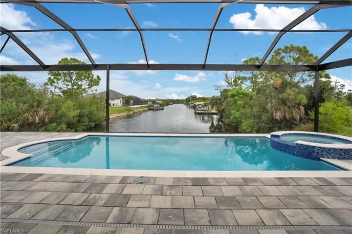 View of swimming pool featuring glass enclosure, a water view, a sunroom, and a pool with connected hot tub