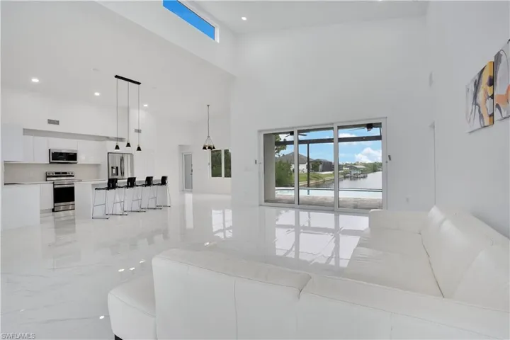 Living area with light marble finish floors, a towering ceiling, a water view, and recessed lighting