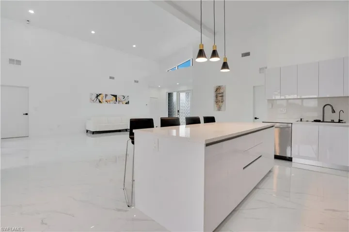 Kitchen featuring a breakfast bar area, modern cabinets, white cabinetry, pendant lighting, and beamed ceiling