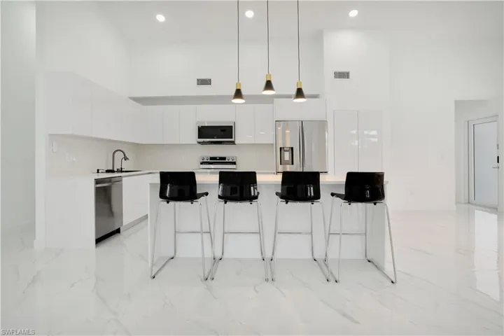 Kitchen featuring a high ceiling, modern cabinets, decorative light fixtures, white cabinets, and stainless steel appliances
