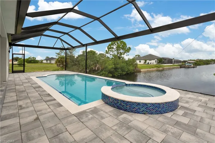 View of swimming pool with a sunroom, a pool with connected hot tub, a patio area, a lanai, and a water view