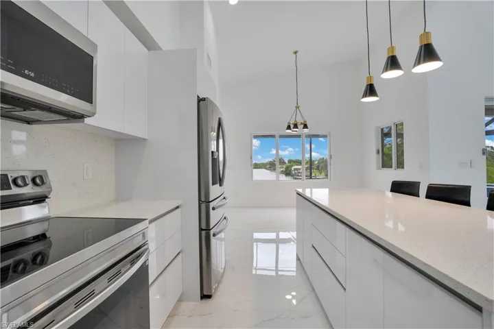 Kitchen with appliances with stainless steel finishes, modern cabinets, white cabinetry, decorative light fixtures, and high vaulted ceiling