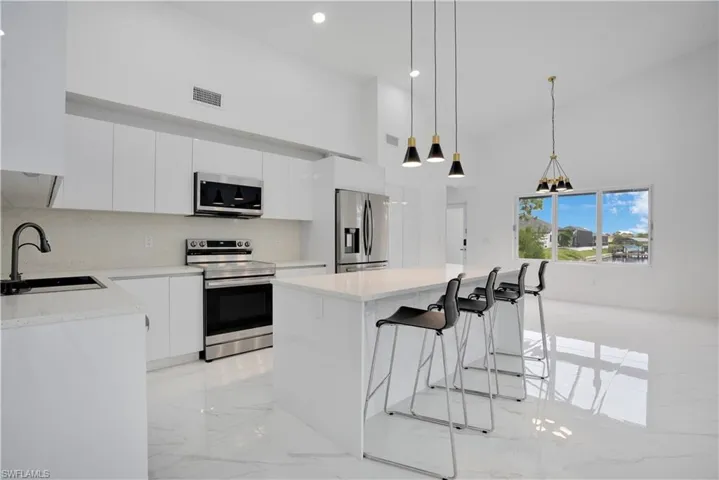Kitchen with a breakfast bar, high vaulted ceiling, appliances with stainless steel finishes, decorative light fixtures, and white cabinets