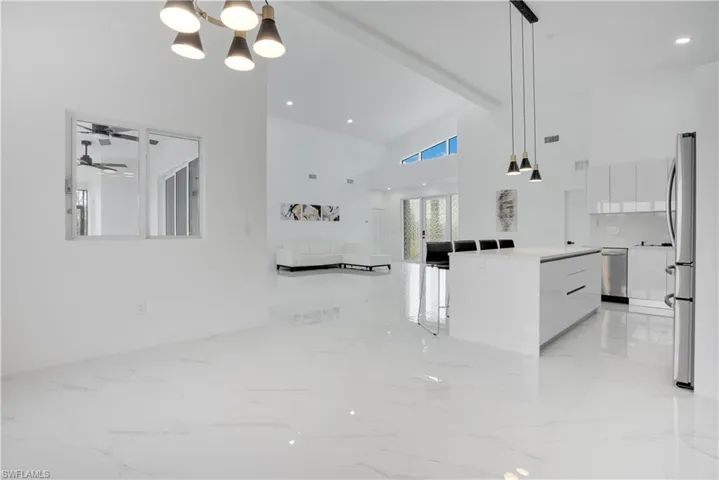 Unfurnished living room with light marble finish floors, a chandelier, beam ceiling, a high ceiling, and recessed lighting