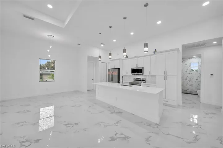 Kitchen featuring decorative light fixtures, a spacious island, appliances with stainless steel finishes, tasteful backsplash, and white cabinets