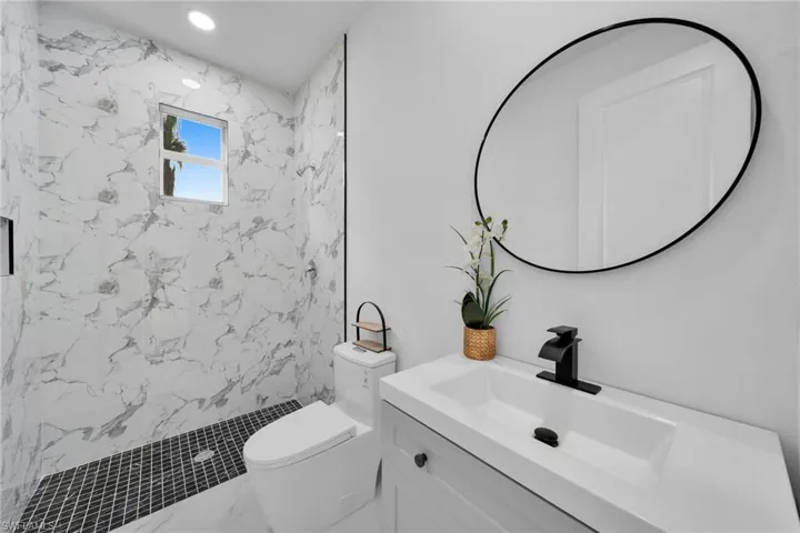 Bathroom with toilet, a tile shower, and vanity