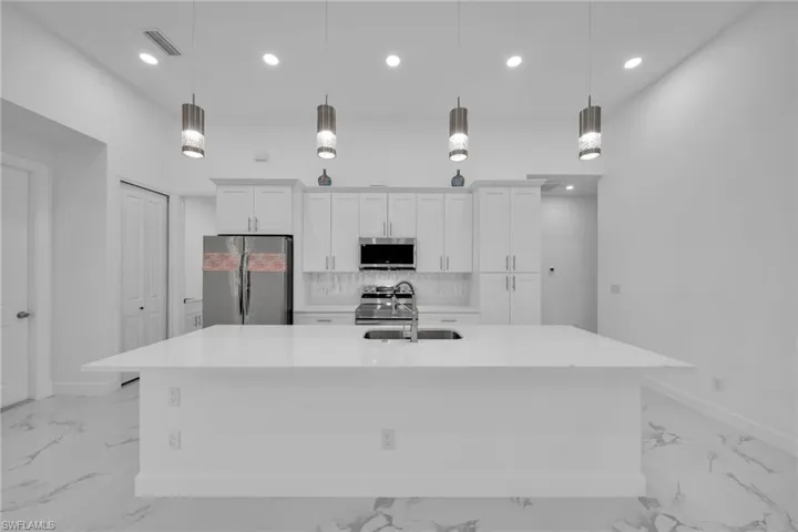 Kitchen featuring a large island with sink, decorative light fixtures, appliances with stainless steel finishes, and white cabinetry