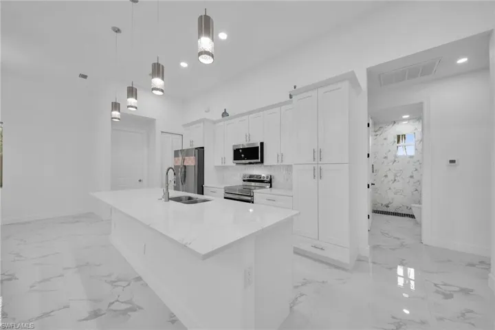 Kitchen featuring appliances with stainless steel finishes, a kitchen island with sink, hanging light fixtures, sink, and white cabinets