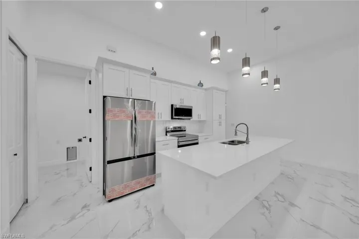 Kitchen featuring decorative light fixtures, appliances with stainless steel finishes, a kitchen island with sink, sink, and white cabinets