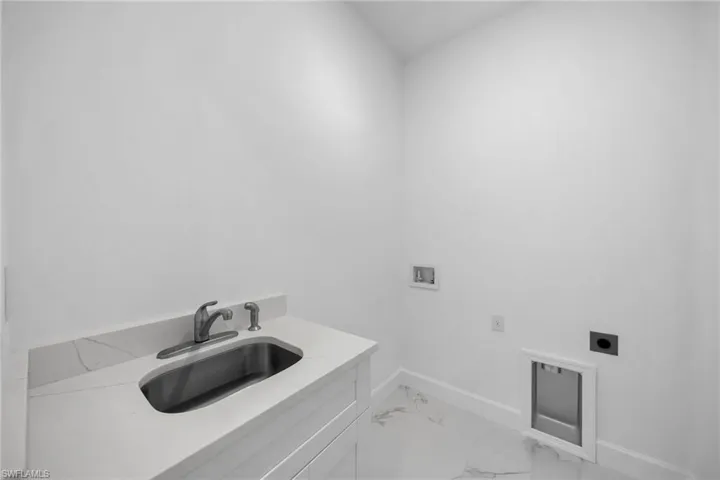 Clothes washing area featuring hookup for a washing machine, cabinets, sink, and hookup for an electric dryer