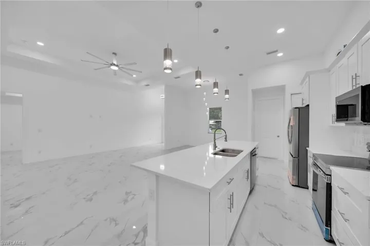 Kitchen featuring a kitchen island with sink, pendant lighting, white cabinetry, stainless steel appliances, and ceiling fan