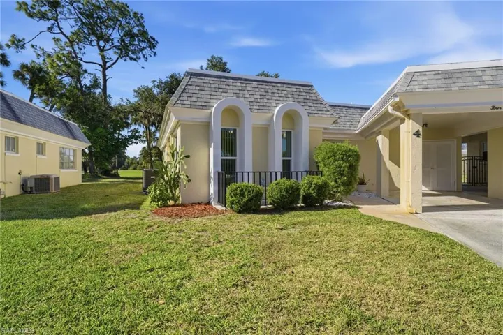 View of home's exterior with a shingled roof, mansard roof, a lawn, a carport, and driveway