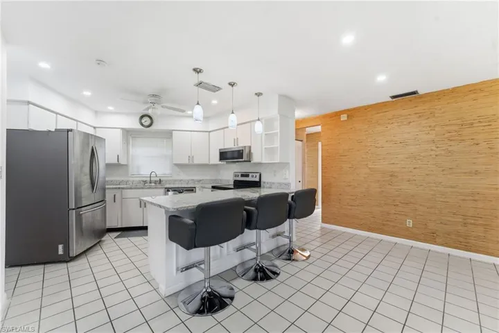 Kitchen with wood walls, open shelves, stainless steel appliances, a breakfast bar area, and hanging light fixtures