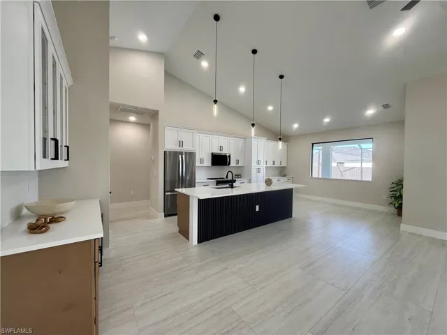 Kitchen featuring dual tone cabinetry, stainless steel appliances, vaulted ceiling, glass insert cabinets, and a kitchen island with sink