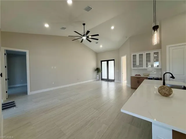 Kitchen featuring a kitchen island with sink, stainless steel appliances, hanging light fixtures, lofted ceiling, and light stone countertops