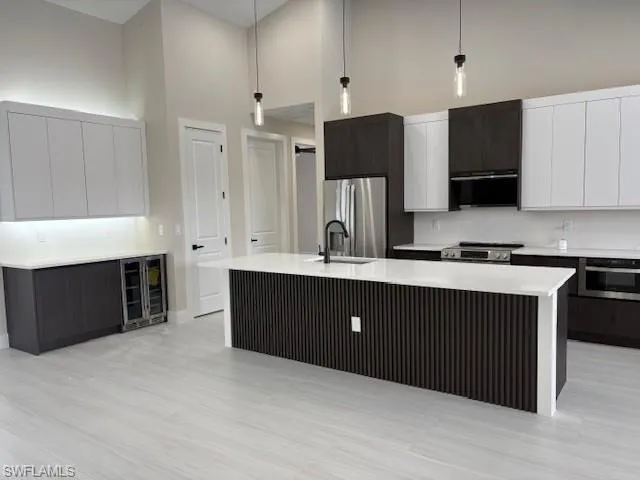 Dual tone kitchen featuring dual tone cabinets, pendant lighting, a kitchen island with sink, a high ceiling, and beverage cooler